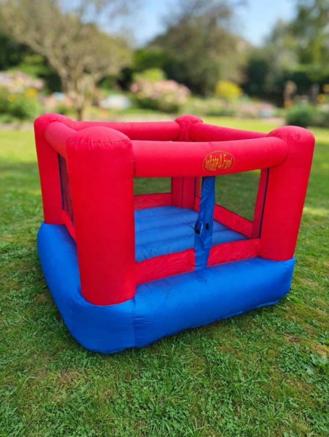 Mini saltarín inflable rojo y azul con mallas laterales, sobre pasto