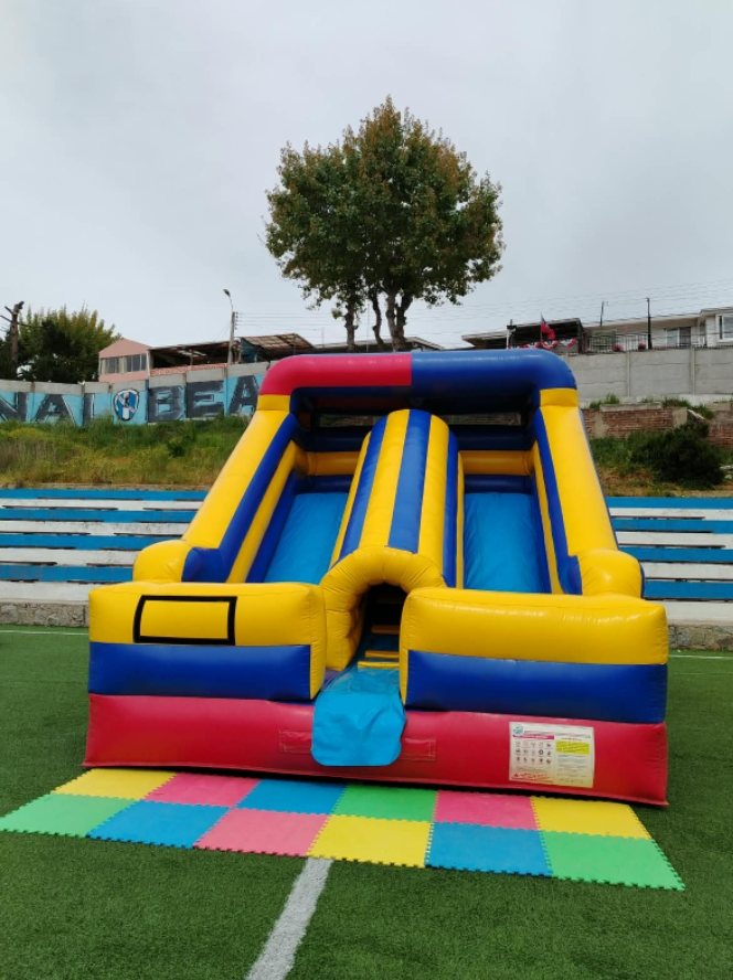 Tobogán inflable doble rojo, amarillo y azul instalado sobre pasto sintético